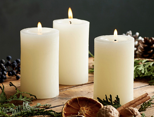3 white pillar candles against a dark background with evergreen and dried orange slices scattered around them